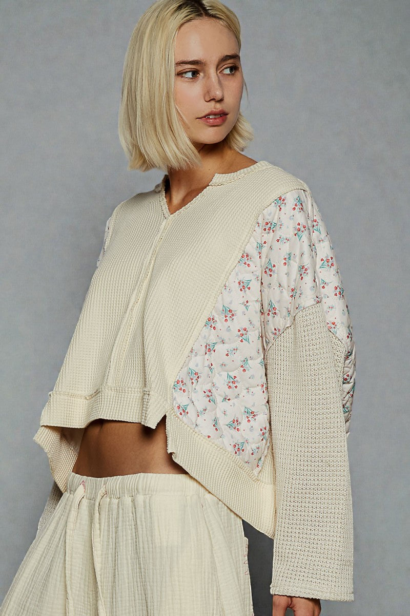 Woman wearing a beige cardigan with floral sleeves against a gray background