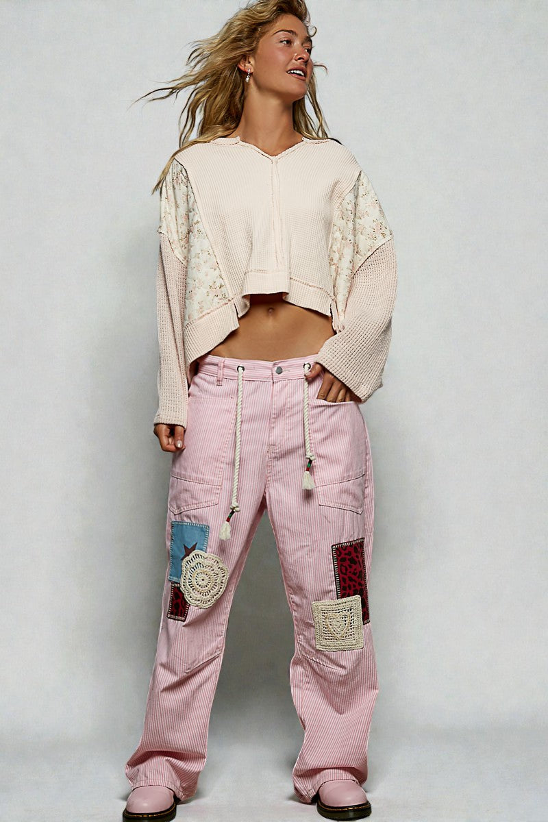 Woman wearing a beige cropped sweater and pink patchwork pants on a white background