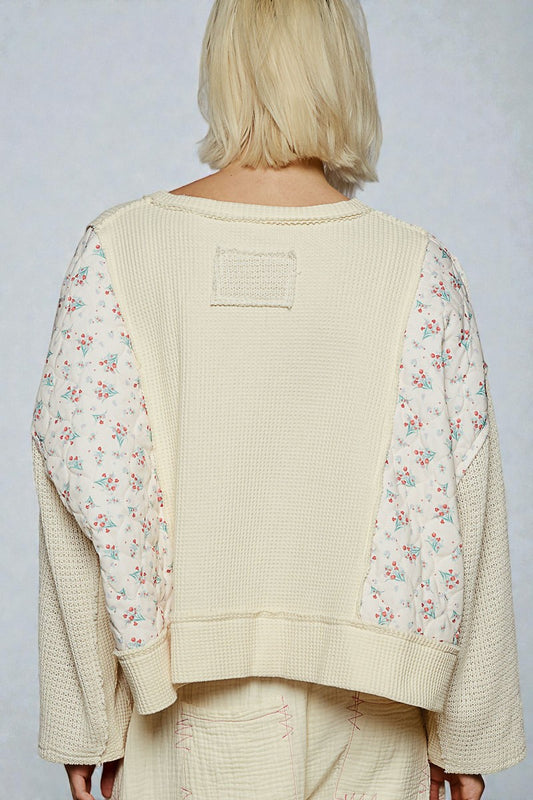 Person wearing a beige sweater with floral sleeves against a plain background