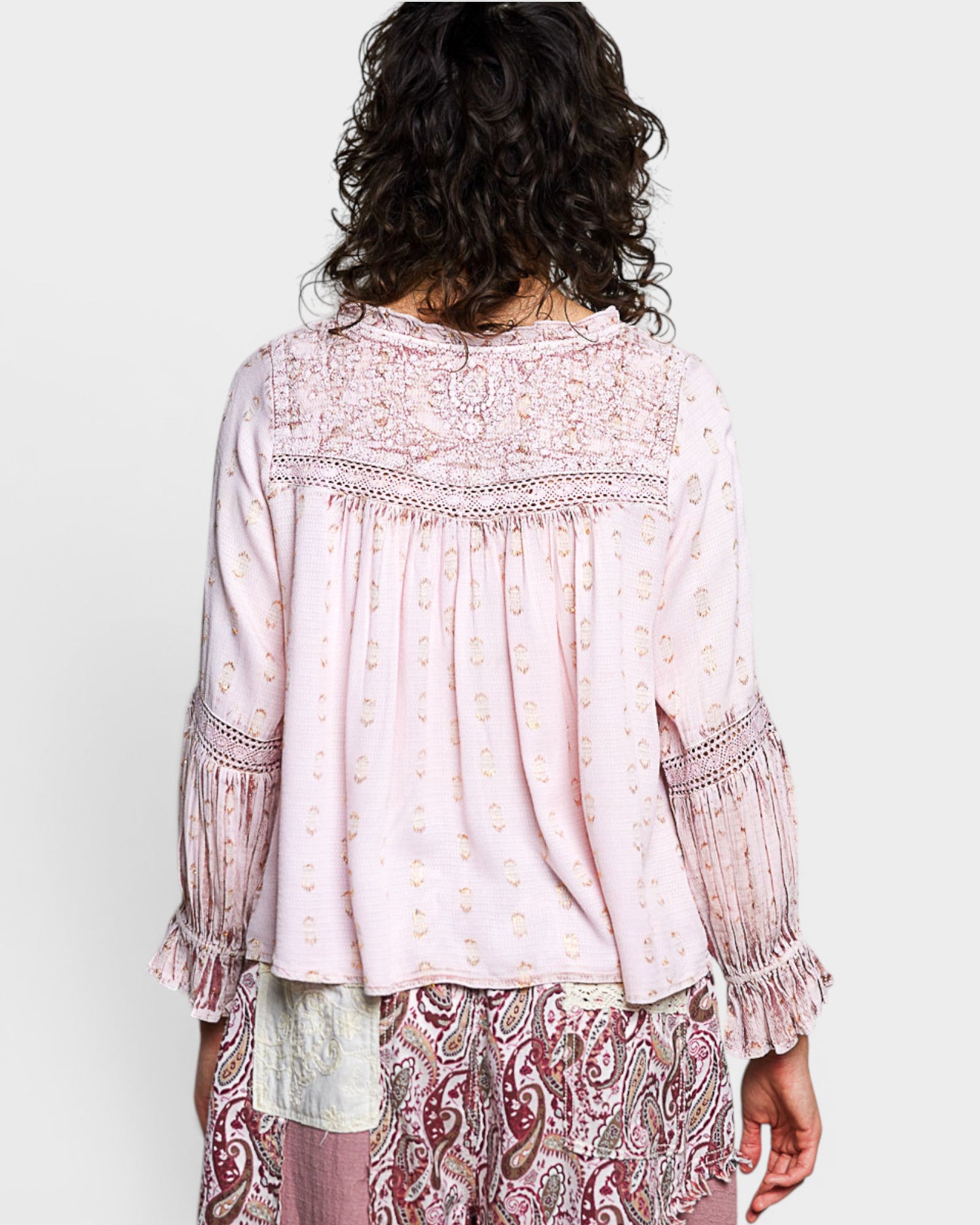 Person wearing a light pink blouse with intricate patterns on a plain background