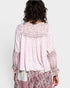 Person wearing a light pink blouse with intricate patterns on a plain background