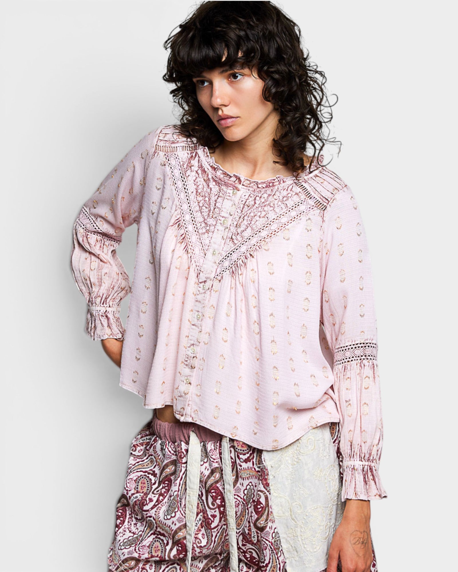 Woman wearing a light pink blouse with intricate patterns on a plain background