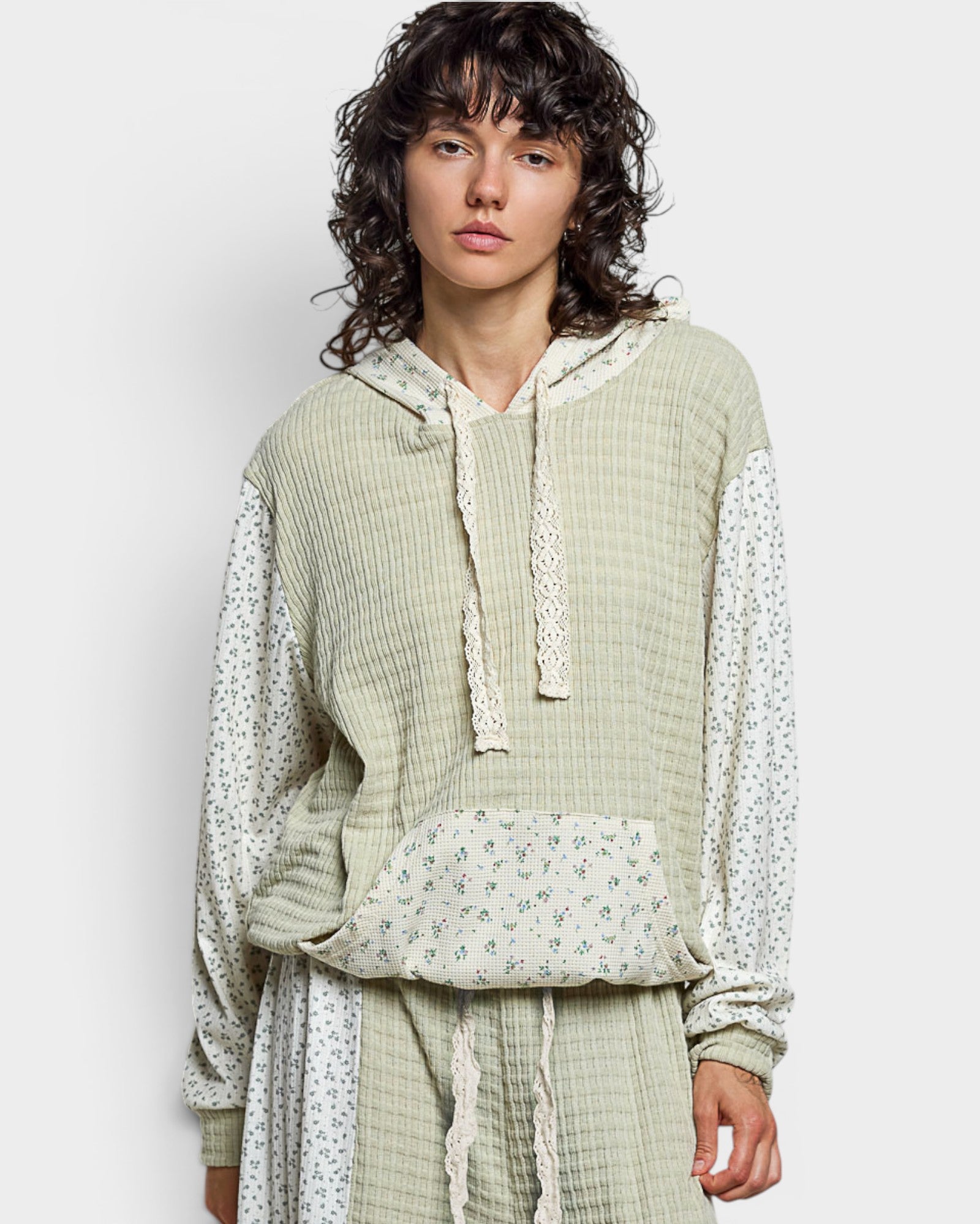 Person wearing a light green textured hoodie with lace details on a plain background
