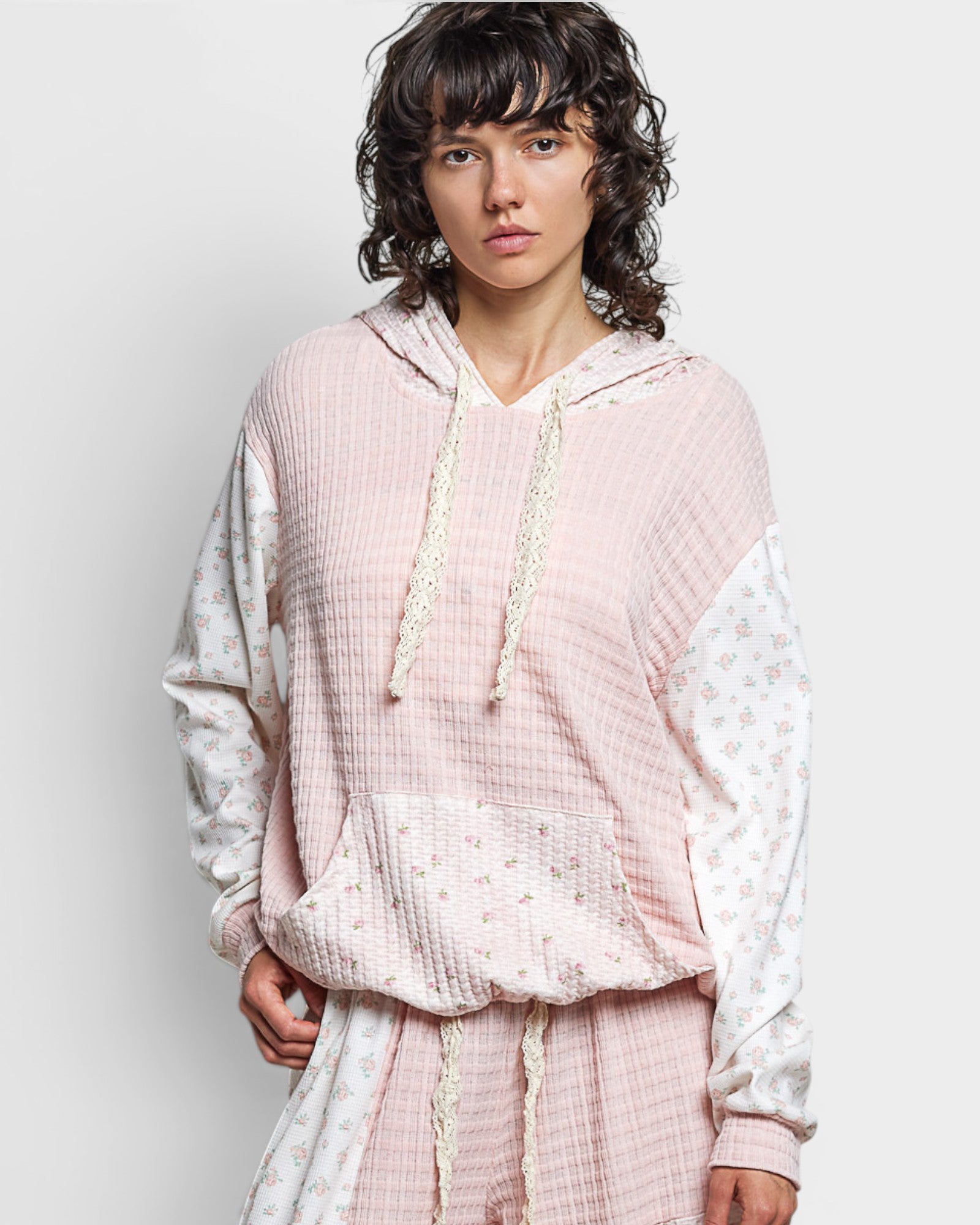 Person wearing a pink textured hoodie and pants on a light gray background