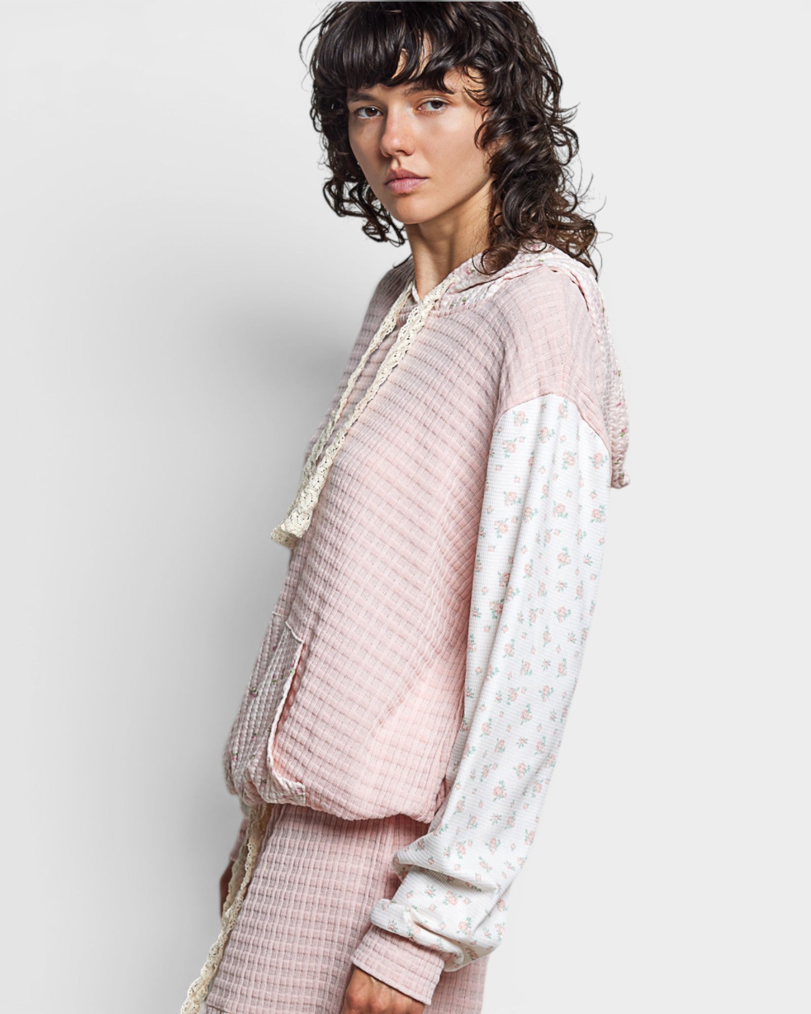 Person wearing a light pink and white outfit with a textured pattern on a plain background