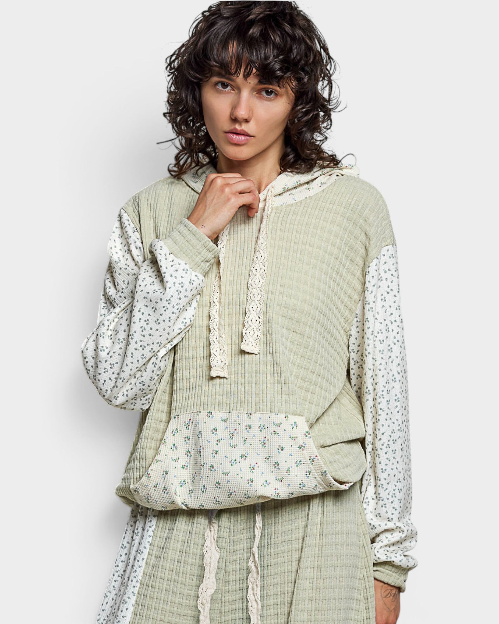 Woman wearing a green textured top with floral sleeves on a white background