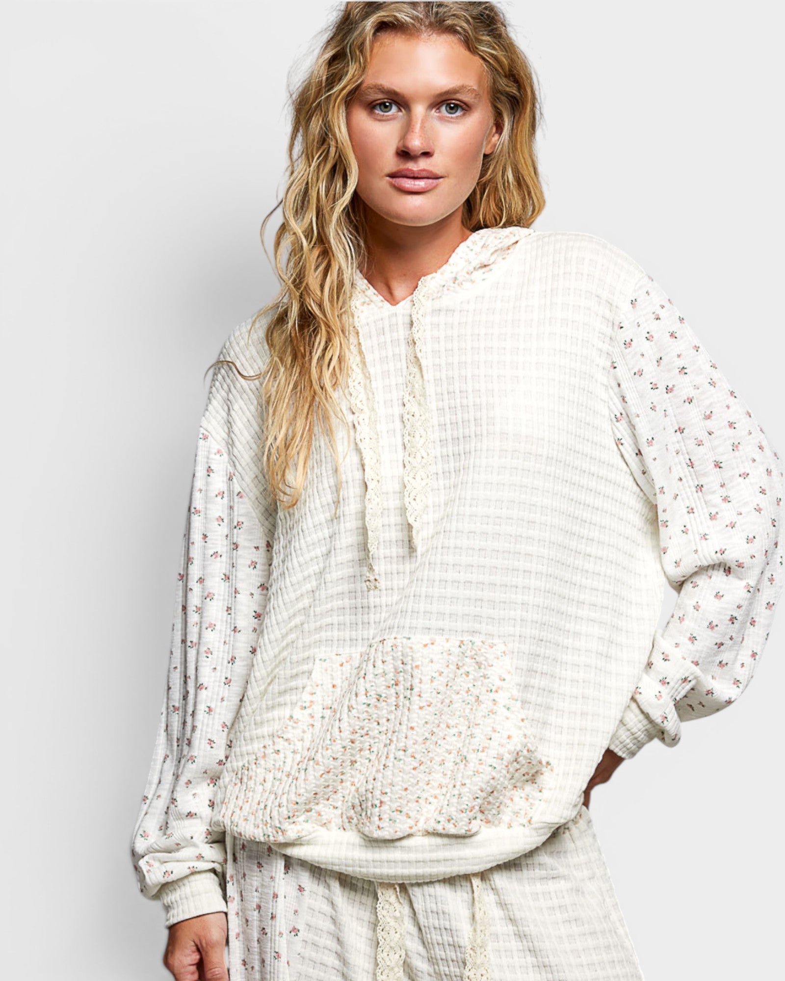 Woman wearing a white textured hoodie and pants on a light gray background