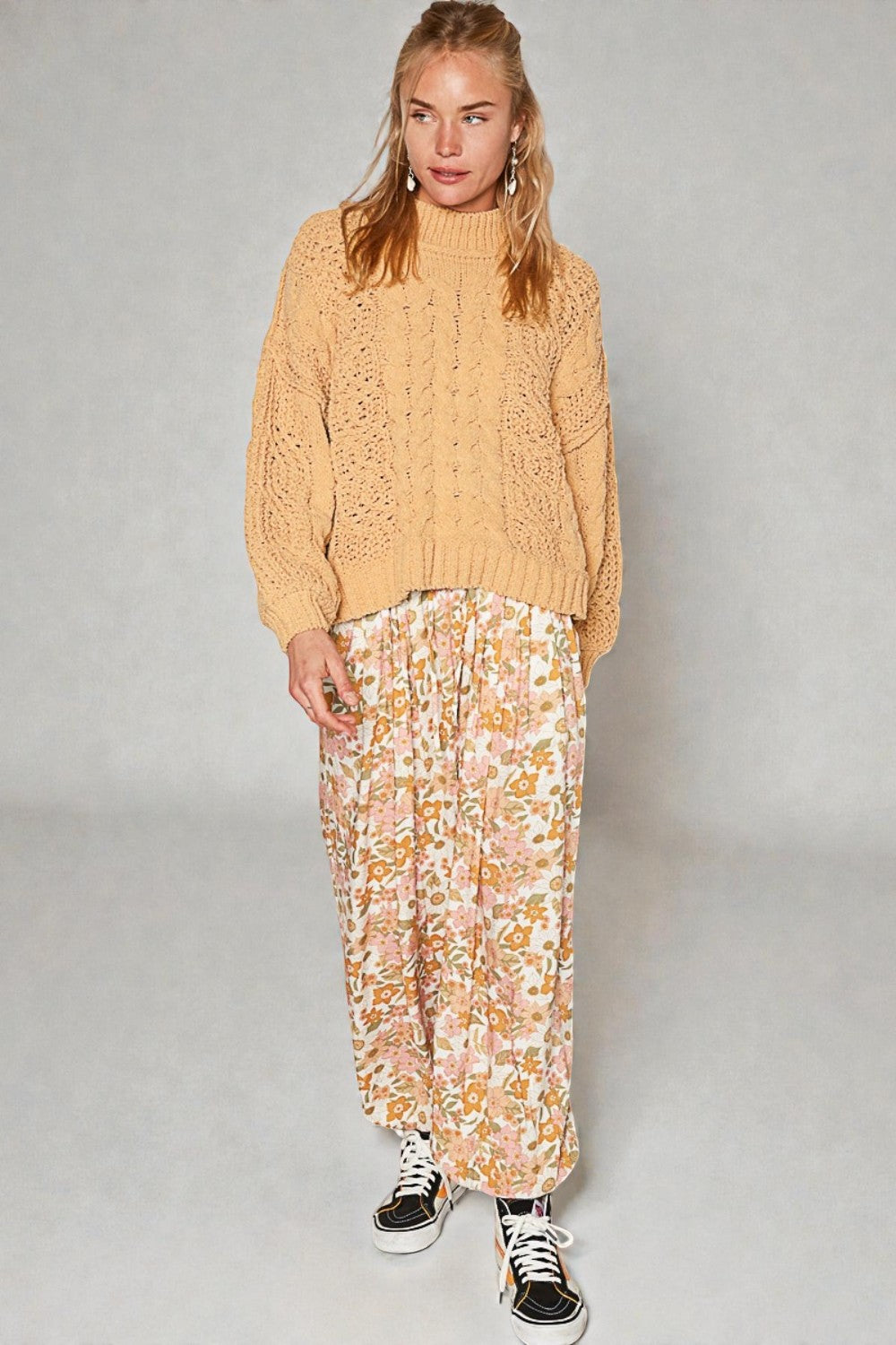 Woman wearing a beige knitted sweater and floral skirt on a gray background