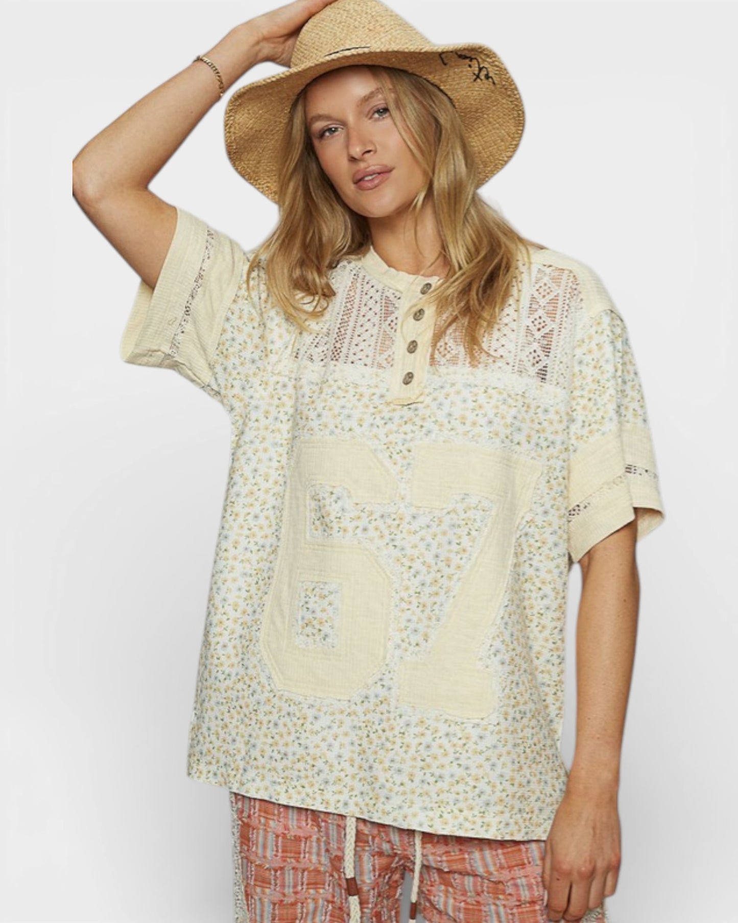 Woman wearing a light-colored lace top and straw hat on a plain background