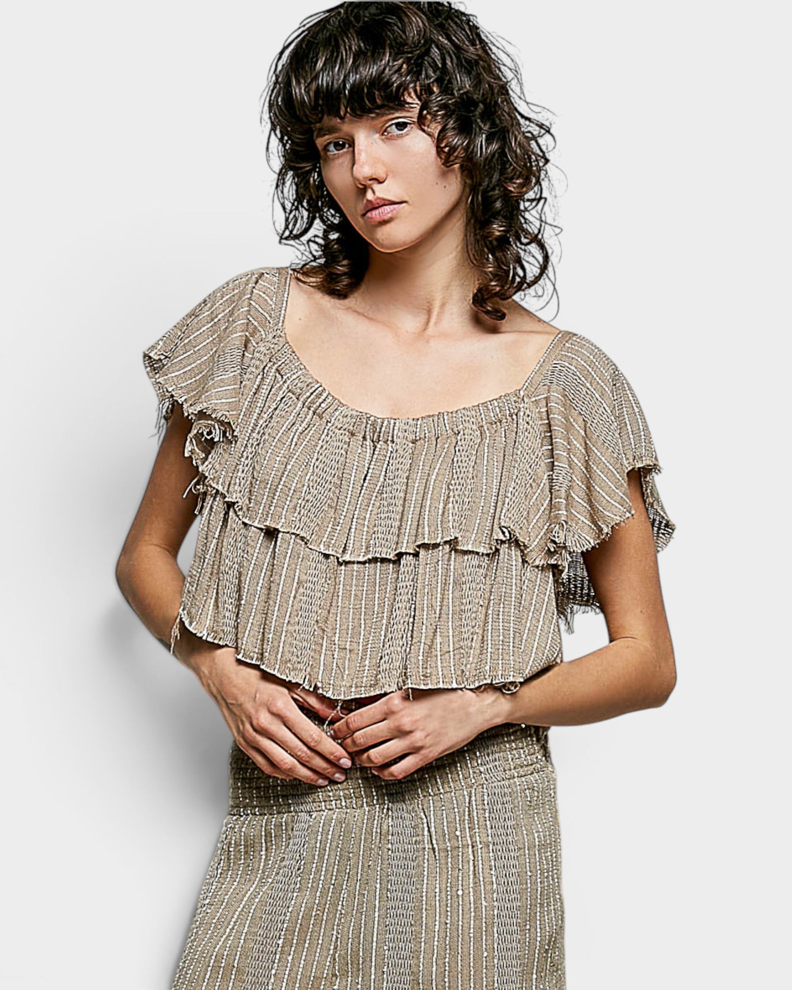 Woman wearing a ruffled top and skirt set against a plain background