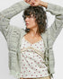 Woman wearing a patterned cardigan with a white top featuring red stars against a plain background