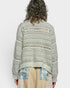 Person wearing a patterned sweater over a plaid shirt and beige pants on a white background