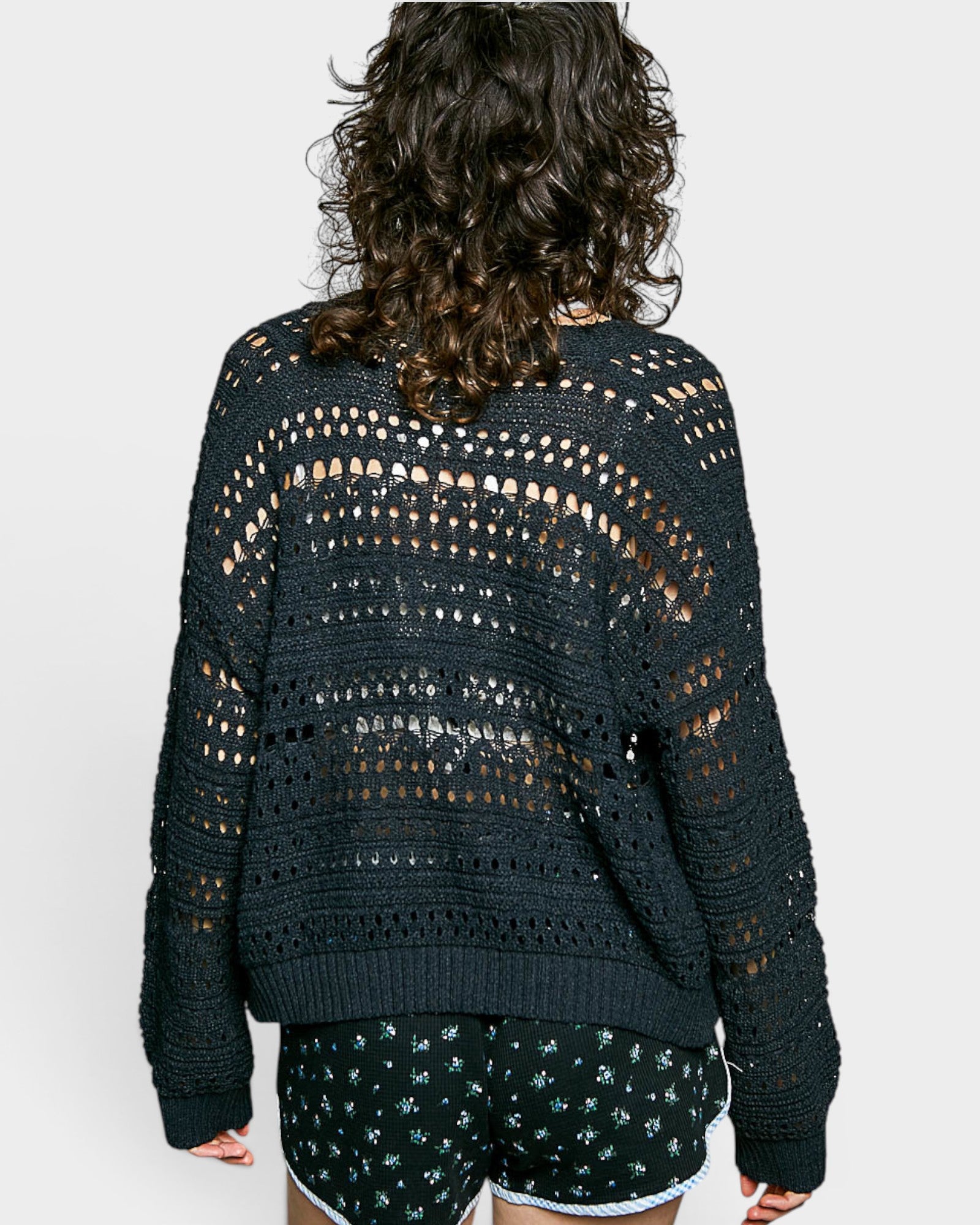 Person wearing a dark green crochet cardigan and shorts on a white background