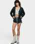 Woman wearing a black cardigan, white top, black shorts with white patterns, and white cowboy boots on a white background.