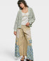 Woman wearing a patterned cardigan, top, and patchwork pants on a white background