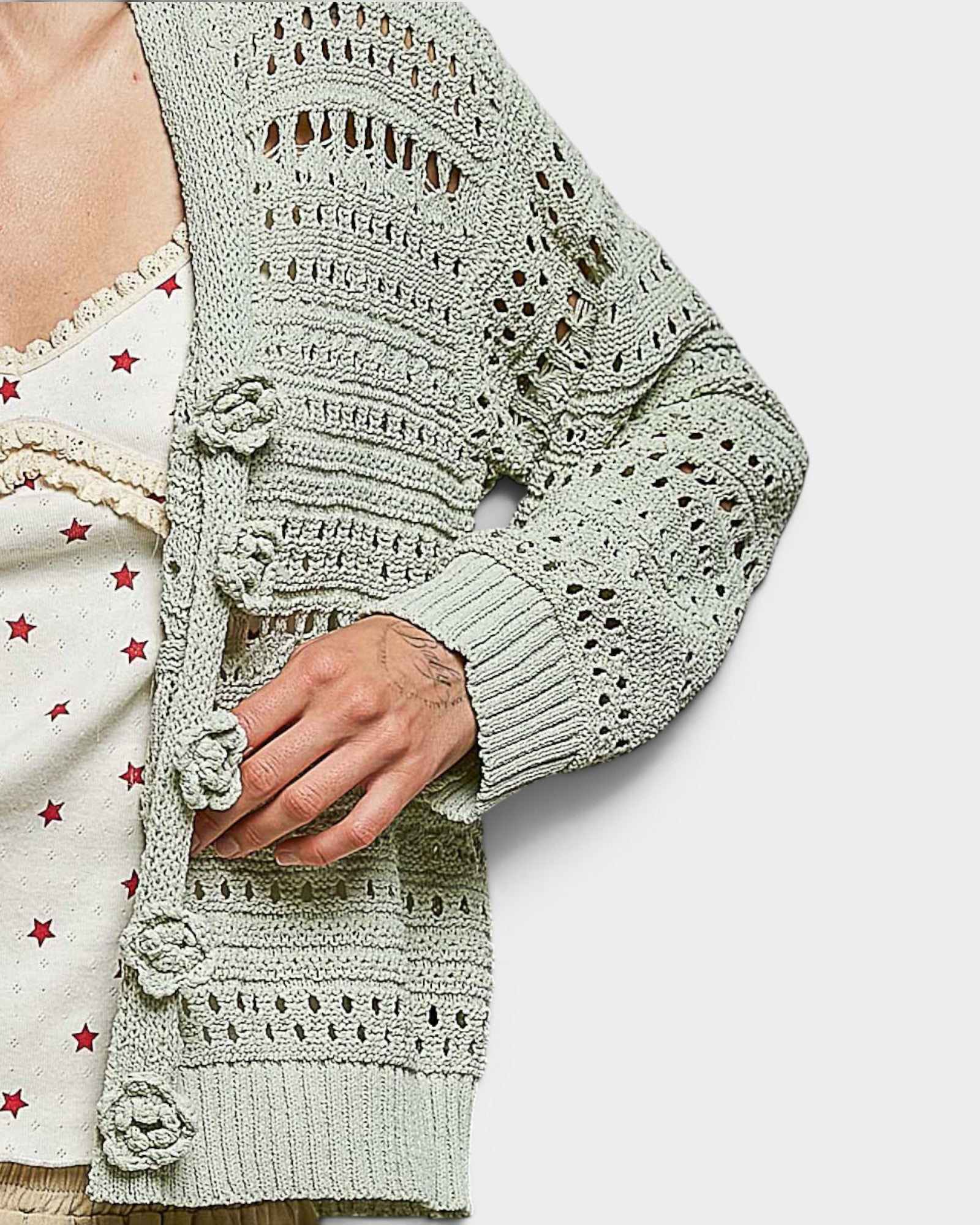 Light green crochet cardigan with decorative buttons on a white background