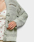 Light green crochet cardigan with decorative buttons on a white background