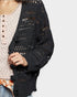 Black open-knit cardigan worn over a patterned top on a light gray background