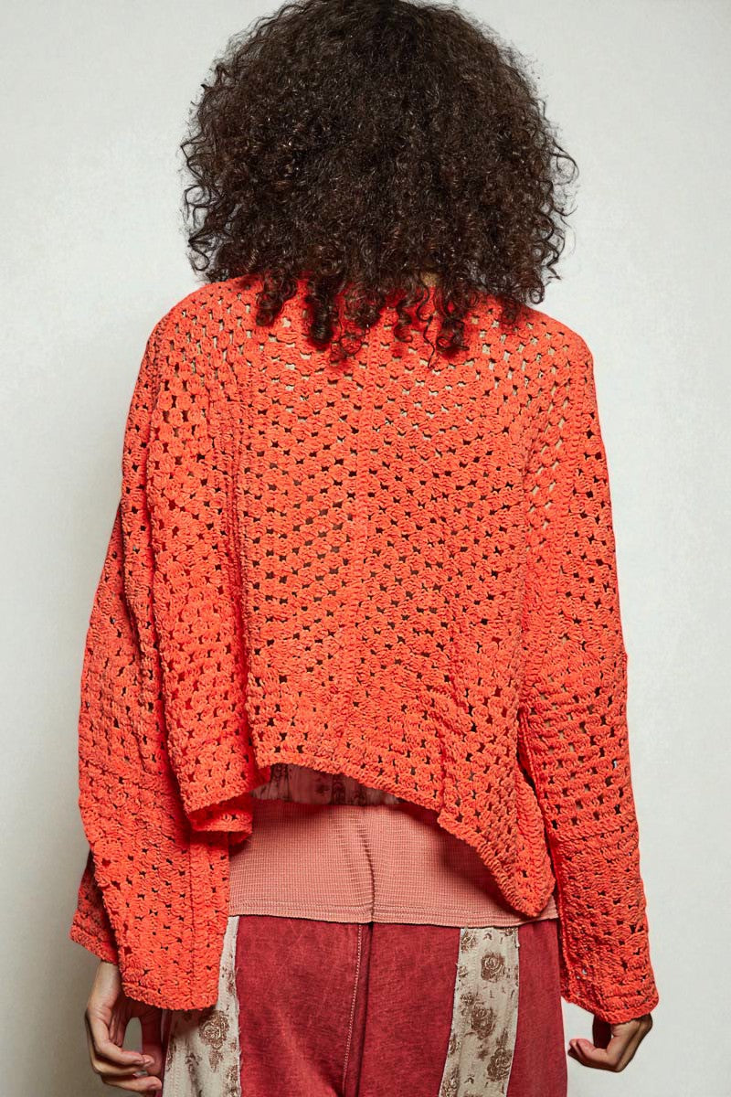 Person wearing a bright orange crochet sweater against a plain background