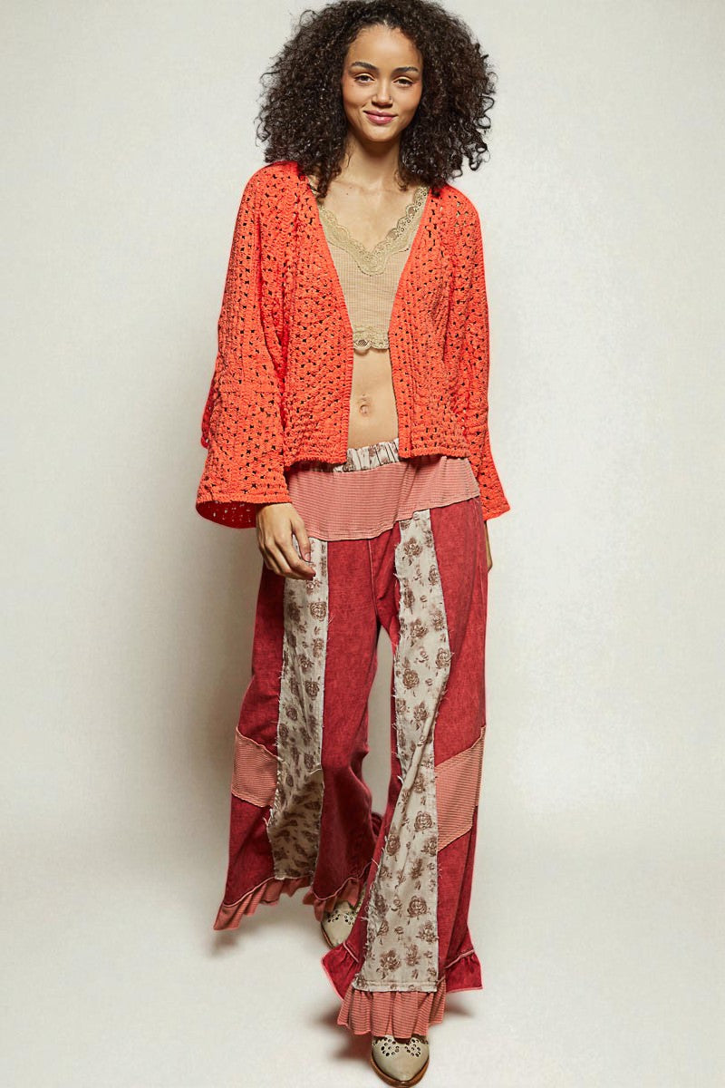 Woman wearing a red patterned outfit with a textured top and floral pants on a plain background