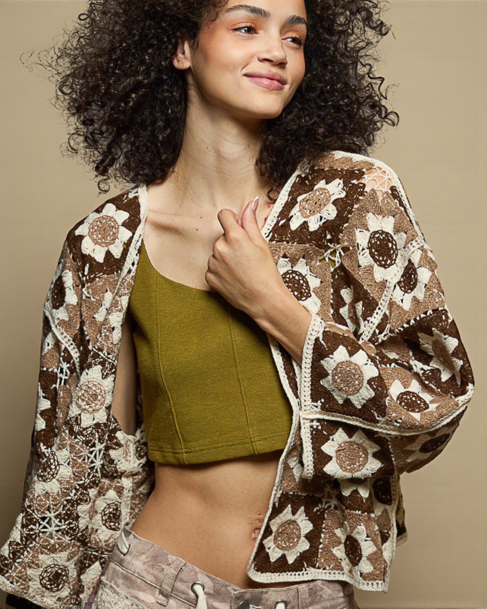 Woman wearing a brown floral-patterned cardigan over a green top against a beige background