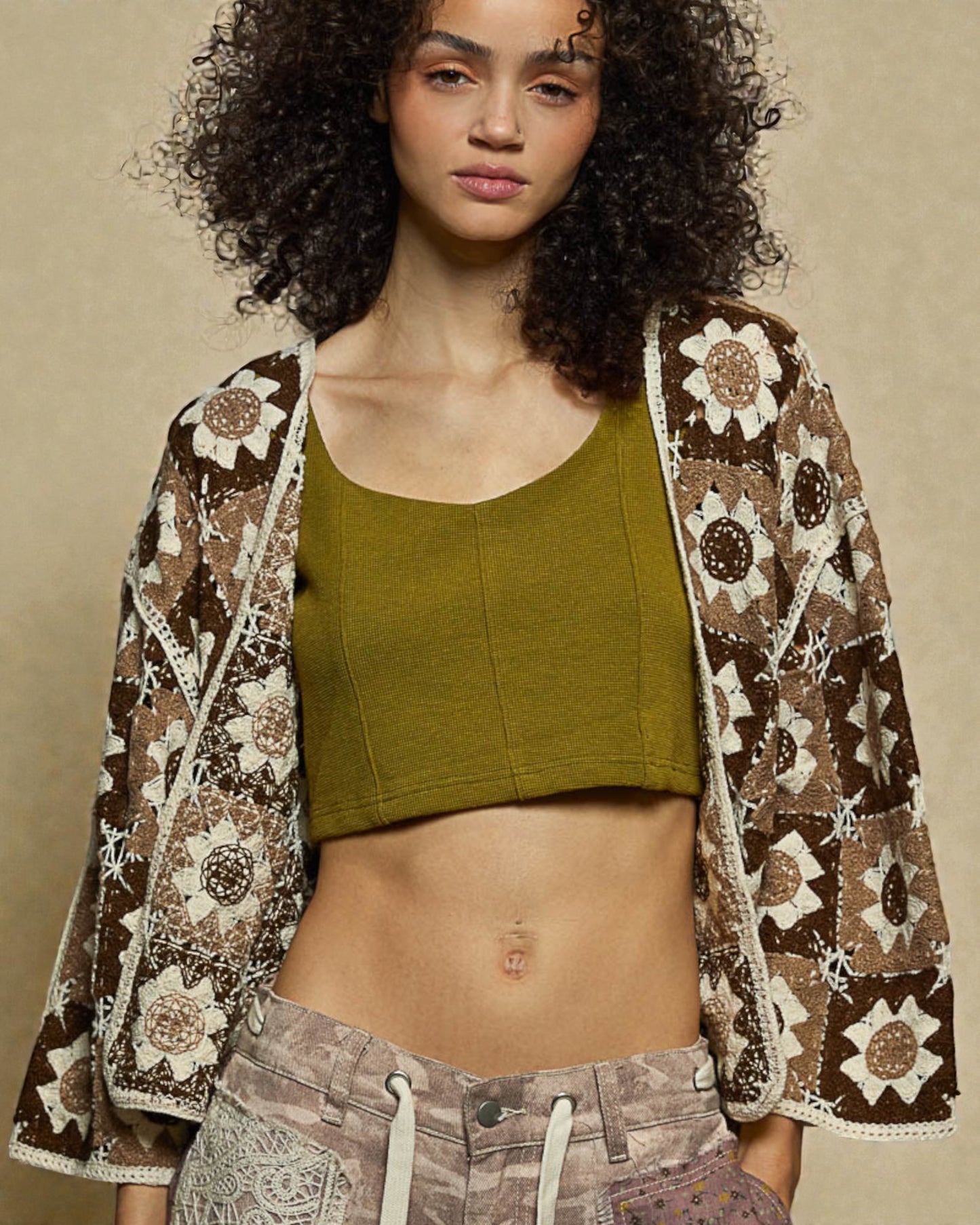 Woman wearing a patterned jacket over a green top and brown pants on a beige background