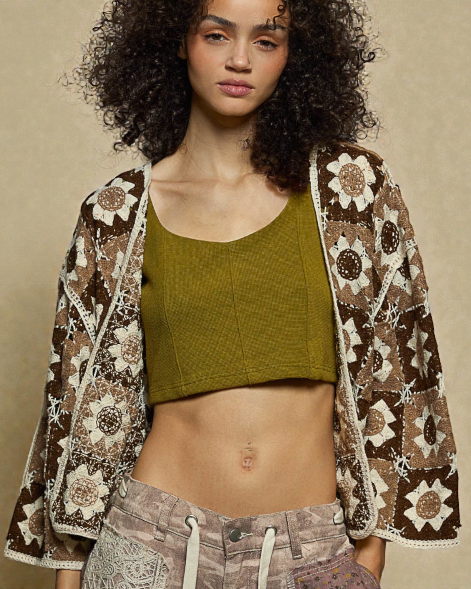 Woman wearing a patterned jacket over a green top and brown pants on a beige background