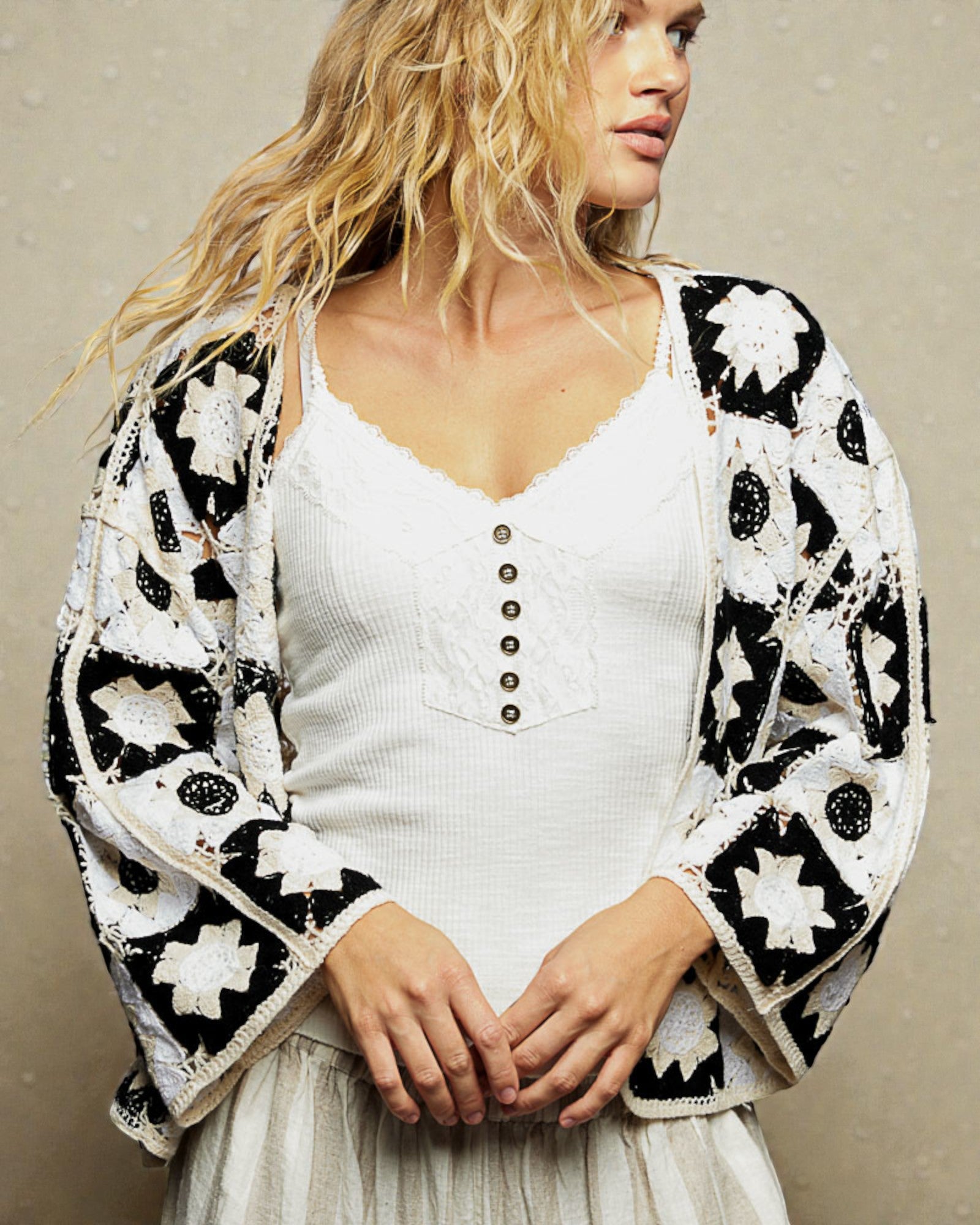 Woman wearing a black and white patterned cardigan over a white top and skirt.