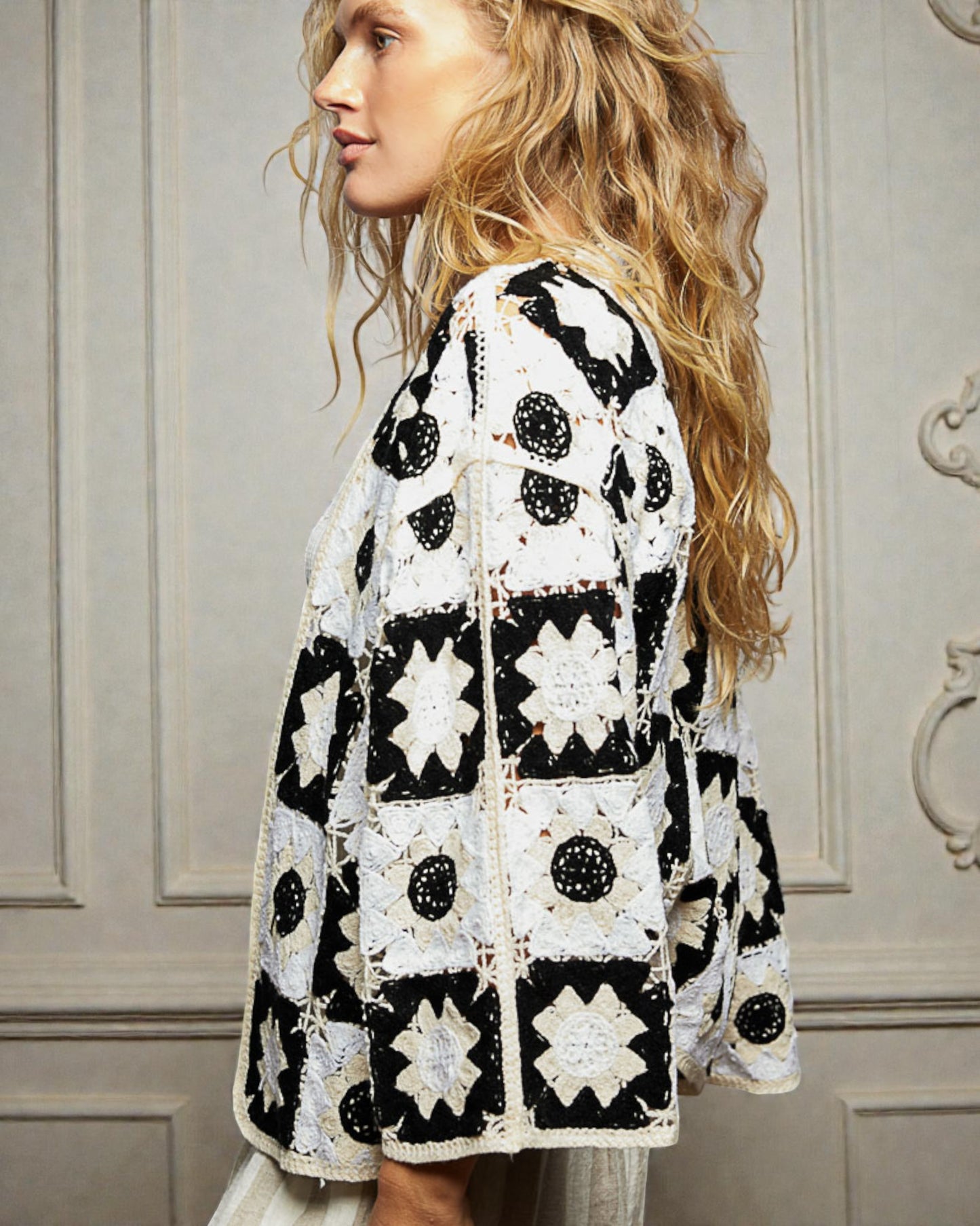 Woman wearing a black and white patterned crochet cardigan against a neutral wall.