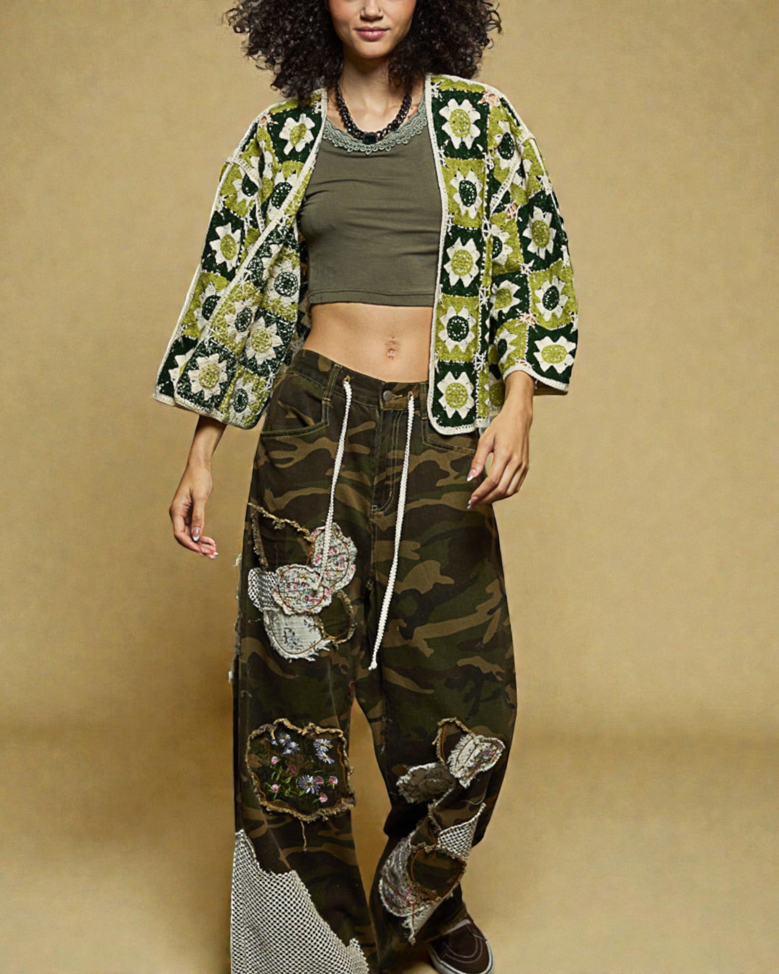 Woman wearing a floral kimono jacket and camouflage pants with patches on a beige background
