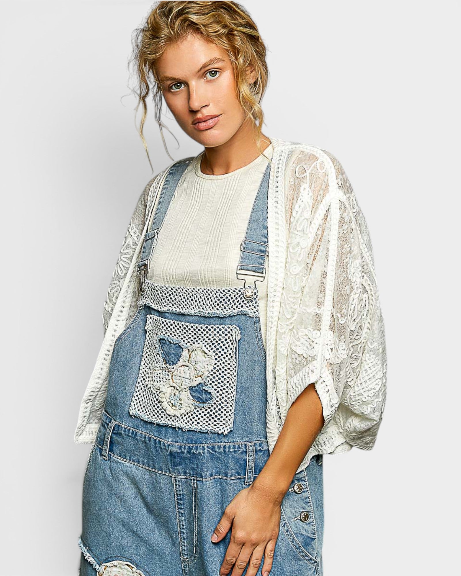 Woman wearing a denim dress with lace details and a white lace cardigan on a light gray background