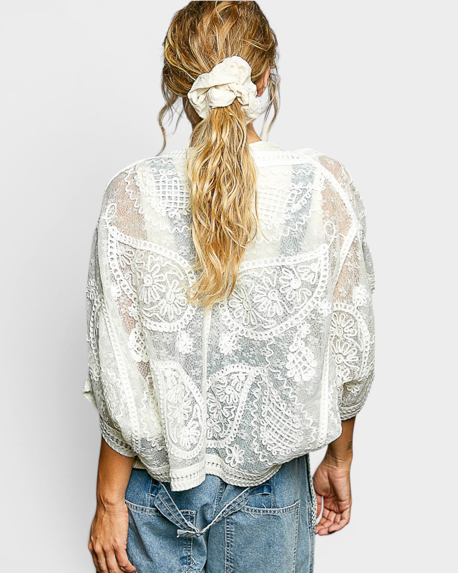 Person wearing a white lace top with blue jeans on a plain background