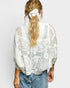 Person wearing a white lace top with blue jeans on a plain background