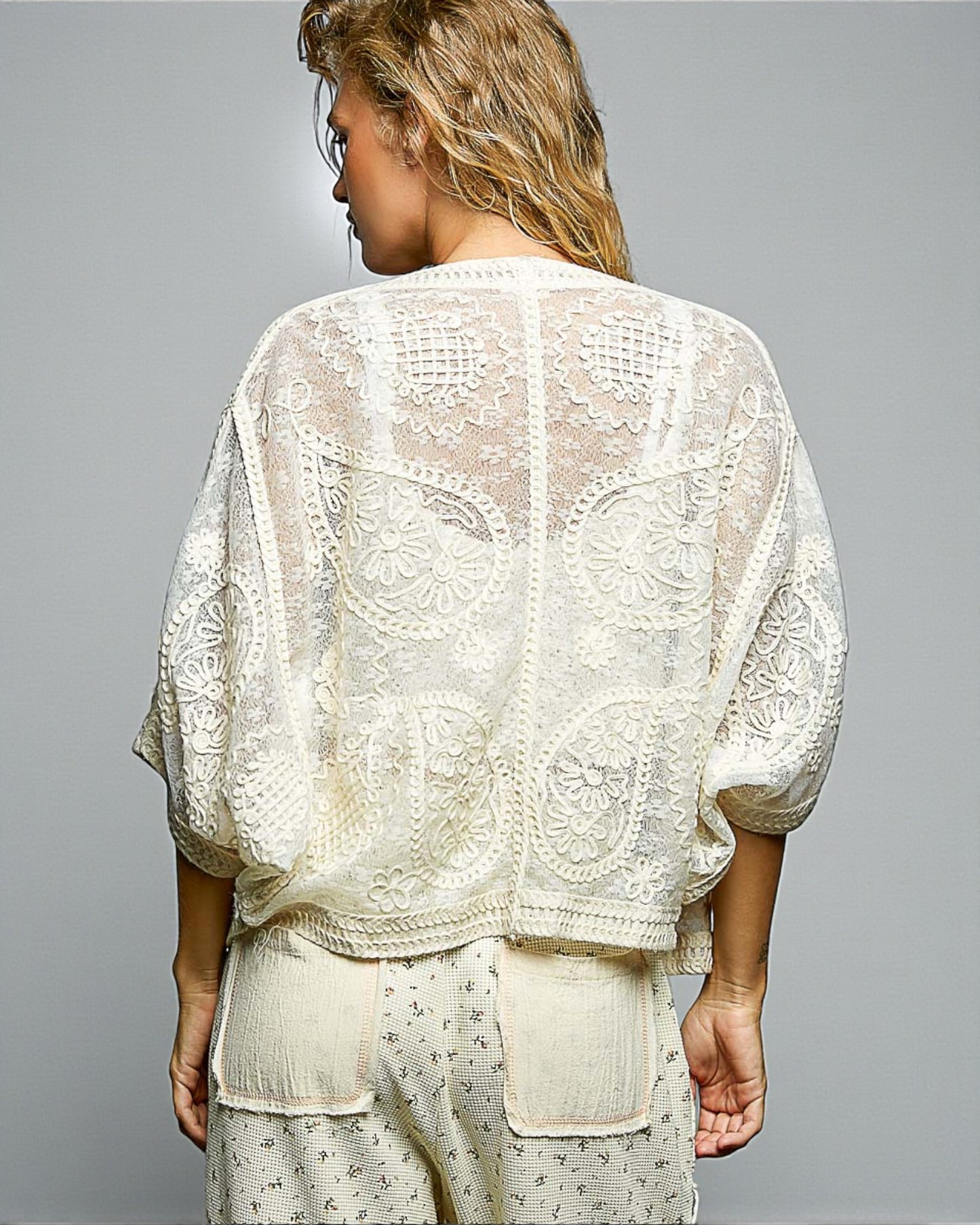 Woman wearing a white lace top and pants against a gray background