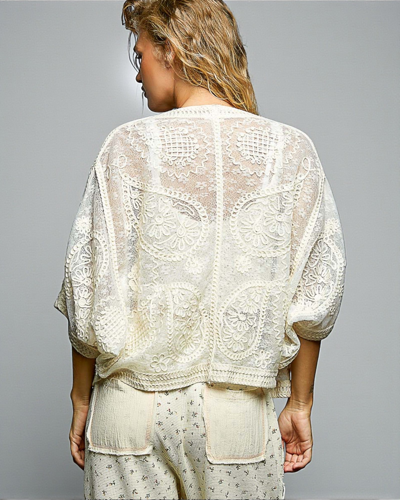 Woman wearing a white lace top and pants against a gray background