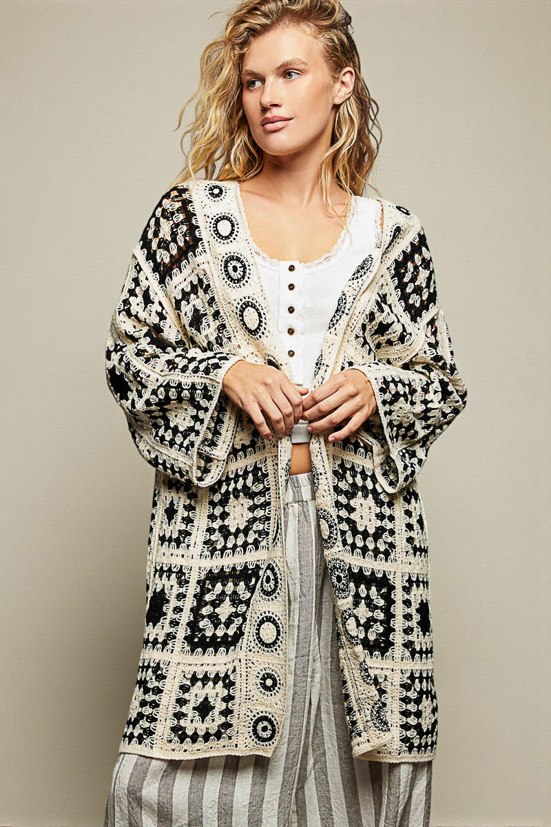 Woman wearing a patterned cardigan over a white shirt and striped pants on a beige background