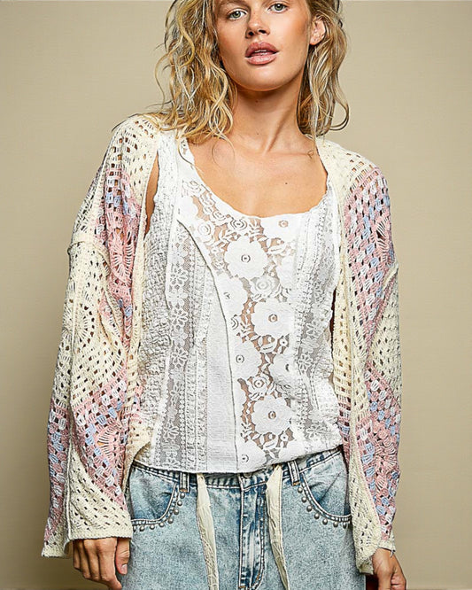 Woman wearing a floral lace top and sheer cardigan against a beige background