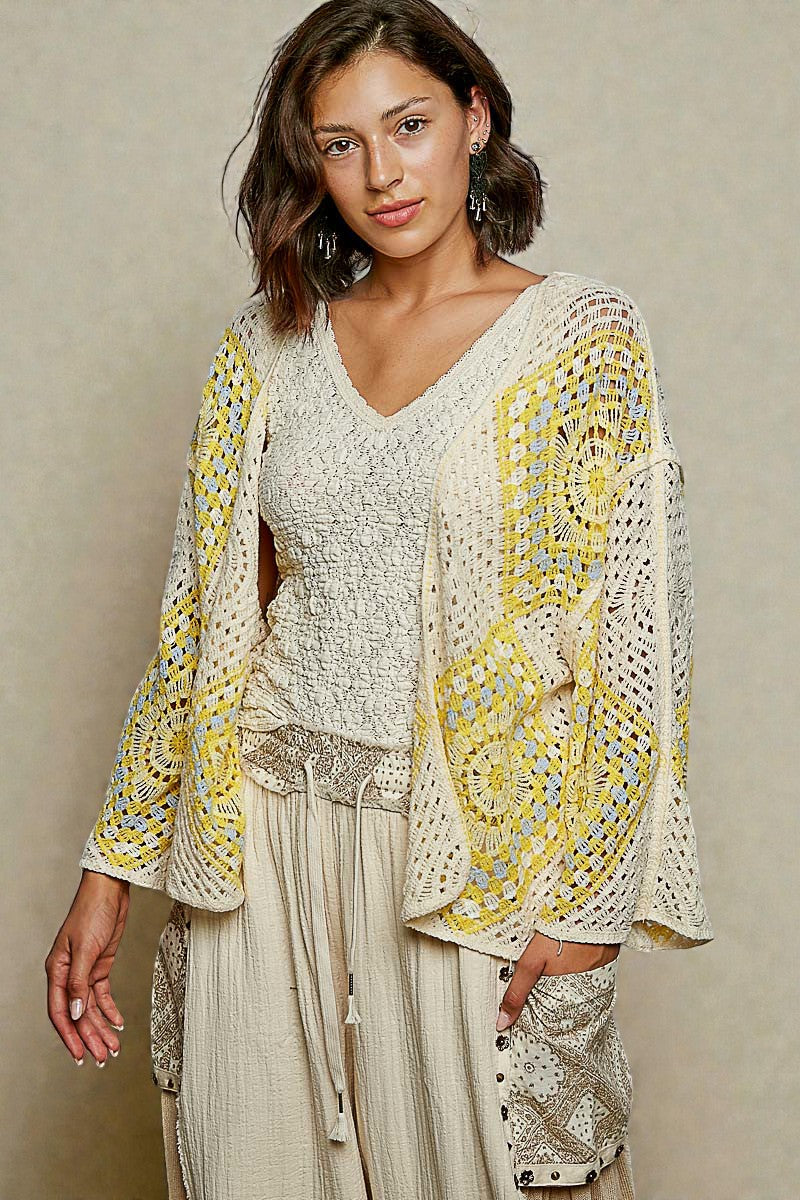 Woman wearing a white and yellow patterned top with beige pants against a neutral background