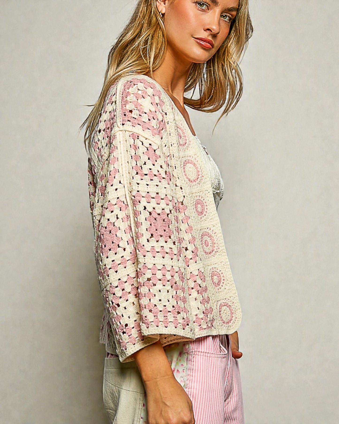 Woman wearing a patterned cardigan and pink pants against a plain background