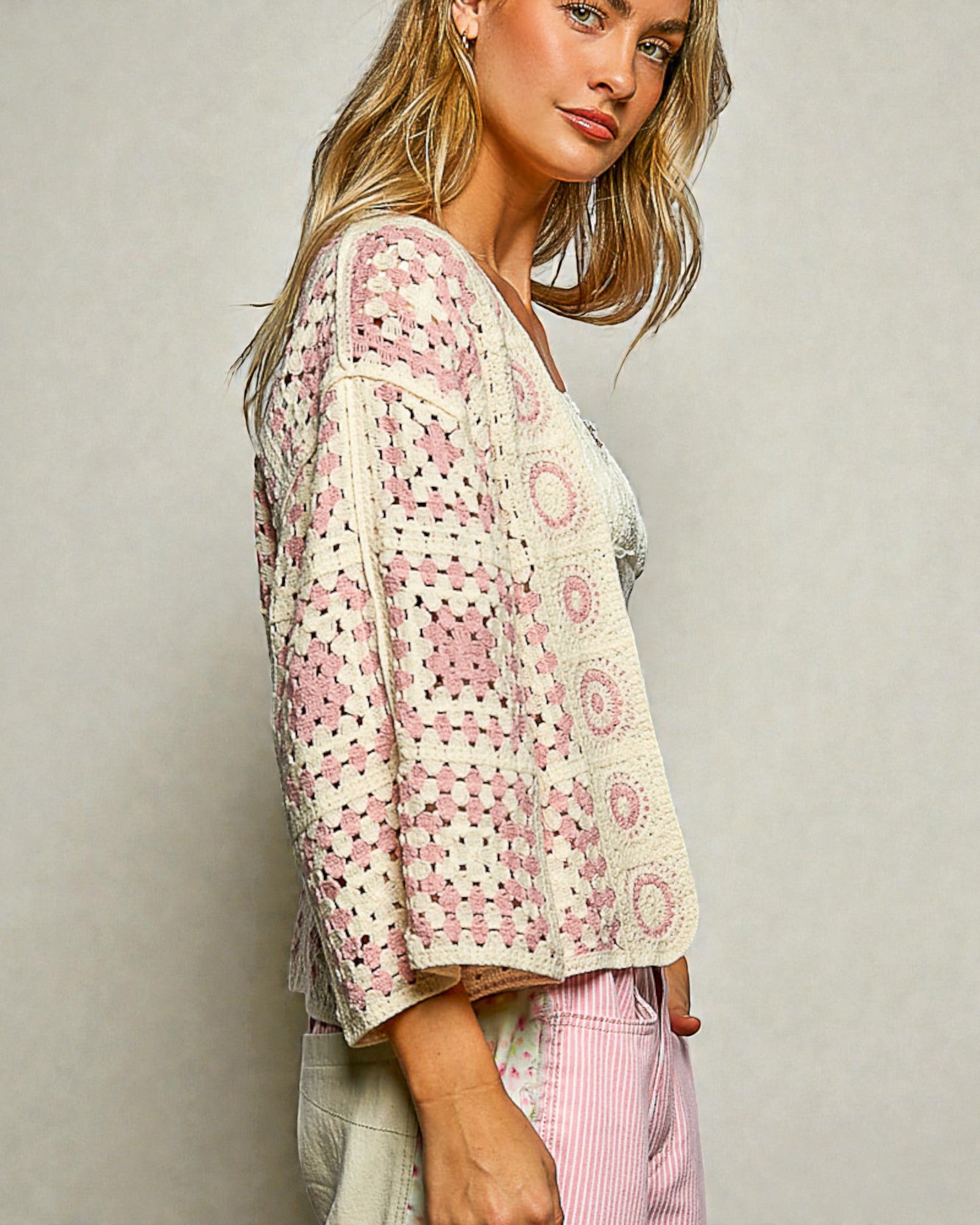 Woman wearing a patterned cardigan and pink pants against a plain background