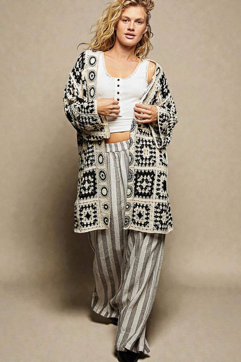 Woman wearing a patterned cardigan and striped pants against a beige background