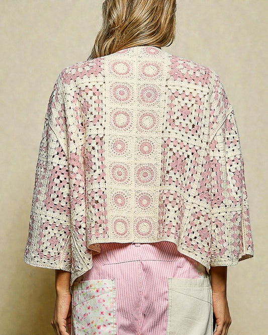 Person wearing a patterned kimono-style jacket over a pink shirt with a beige background