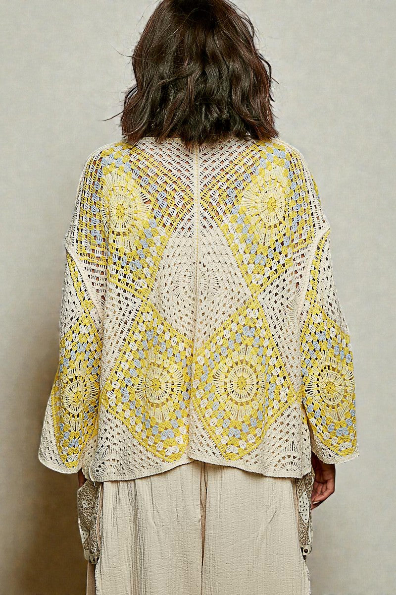 Person wearing a yellow and white patterned crochet top against a neutral background