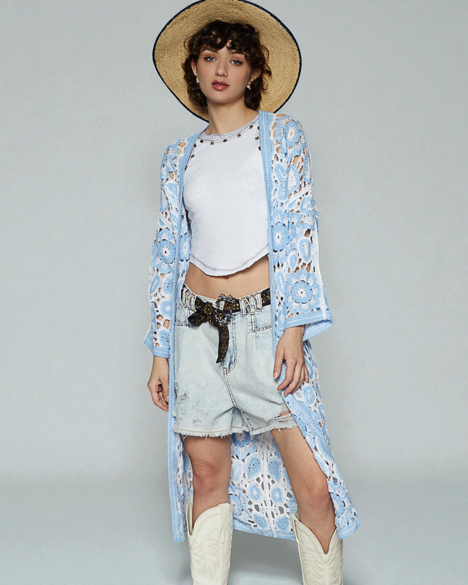 Woman wearing a light blue floral kimono over a white top and denim shorts, standing against a plain background.