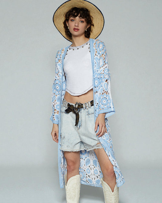 Woman wearing a light blue floral kimono over a white top and denim shorts, standing against a plain background.