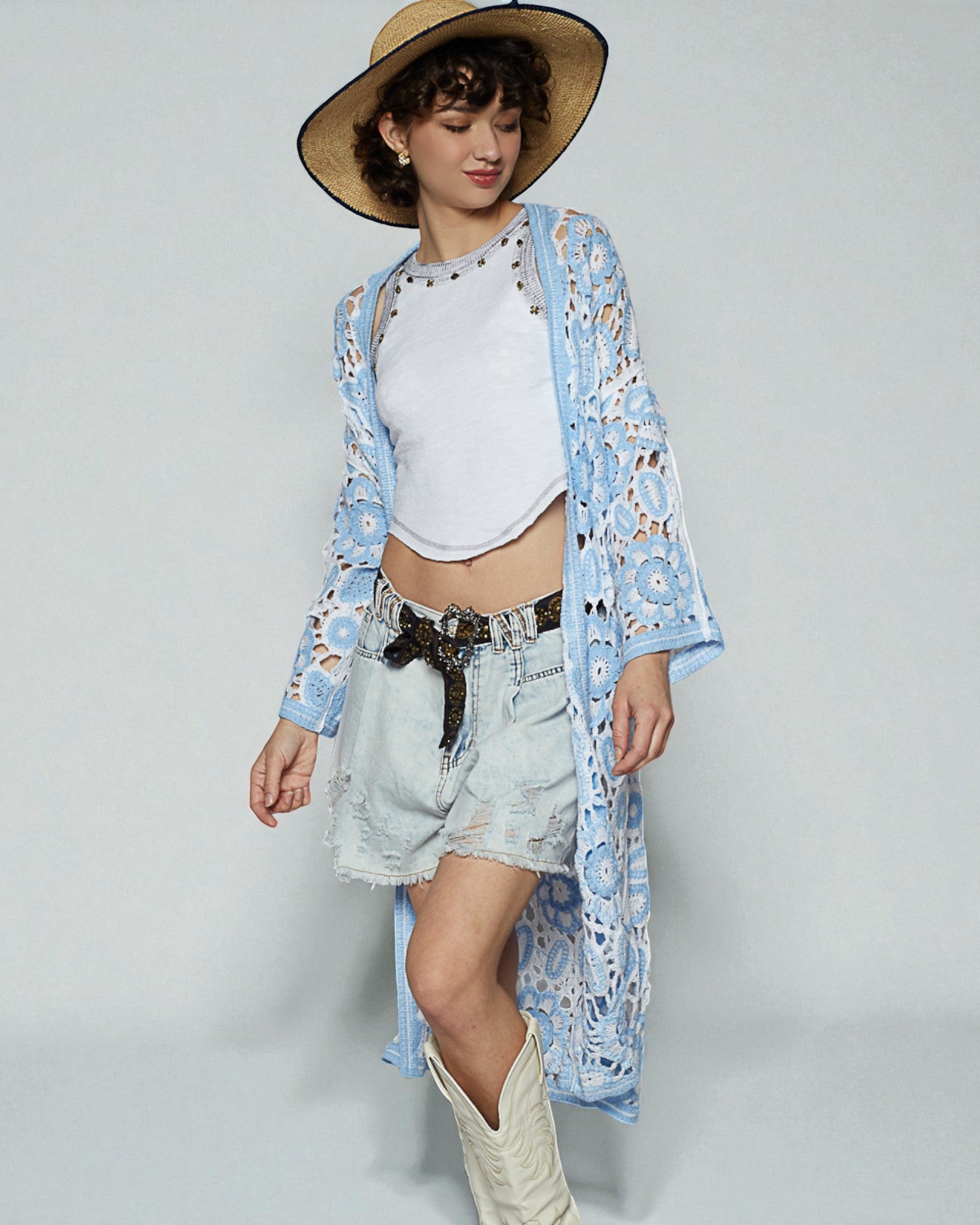 Woman wearing a floral kimono, white top, denim shorts, and white boots on a plain background