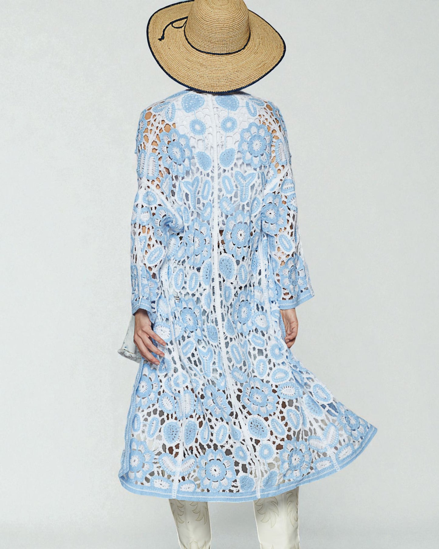 Person wearing a light blue floral dress with a straw hat on a white background