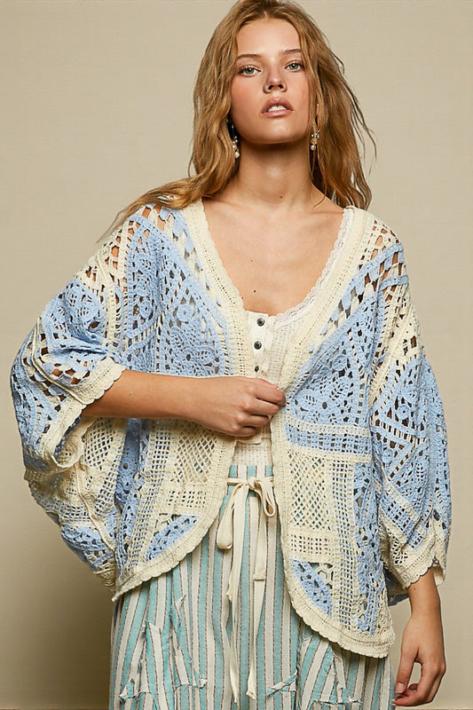 Woman wearing a blue and white crochet cardigan over a striped dress against a beige background