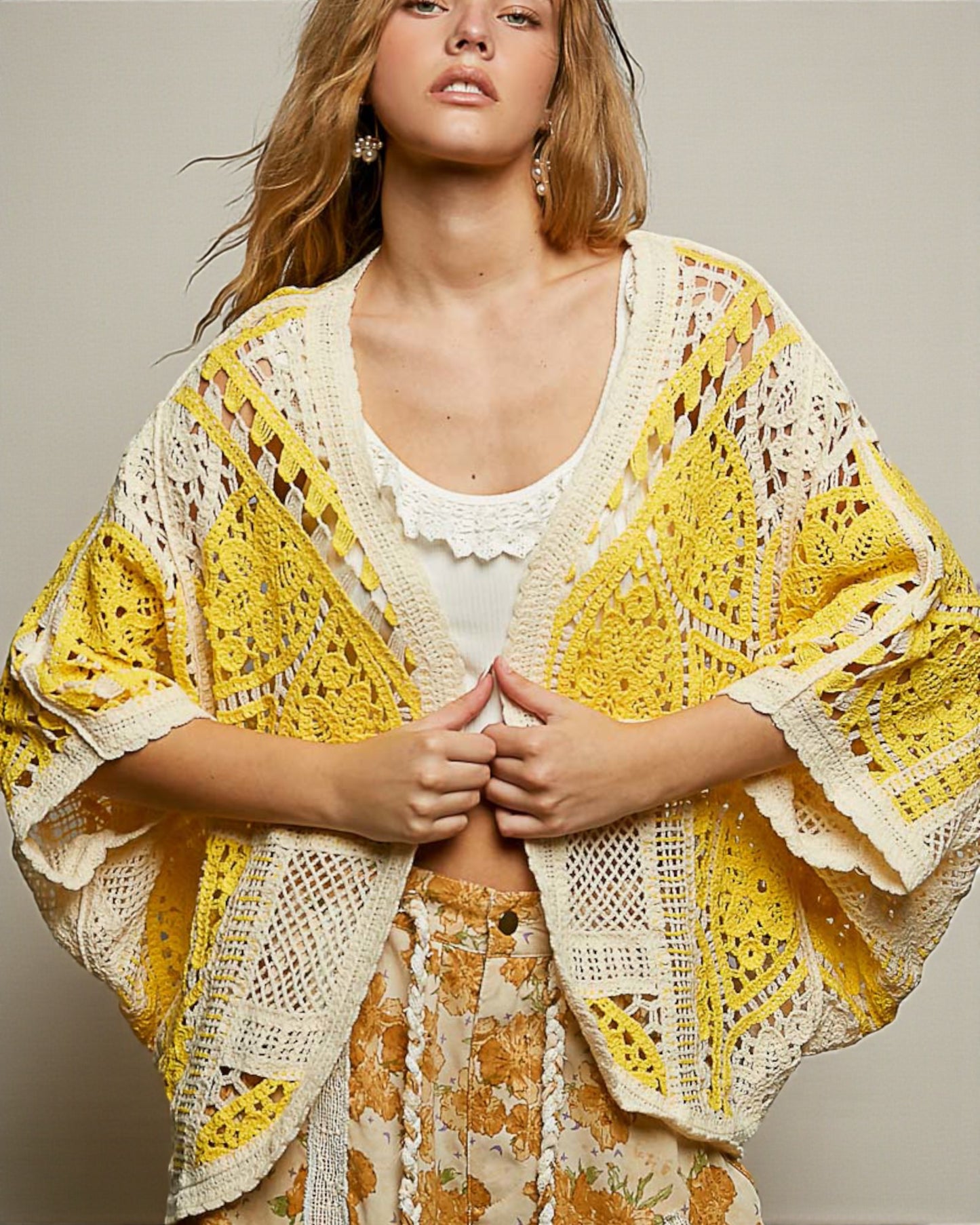 Woman wearing a yellow and white crochet cover-up over a floral dress.