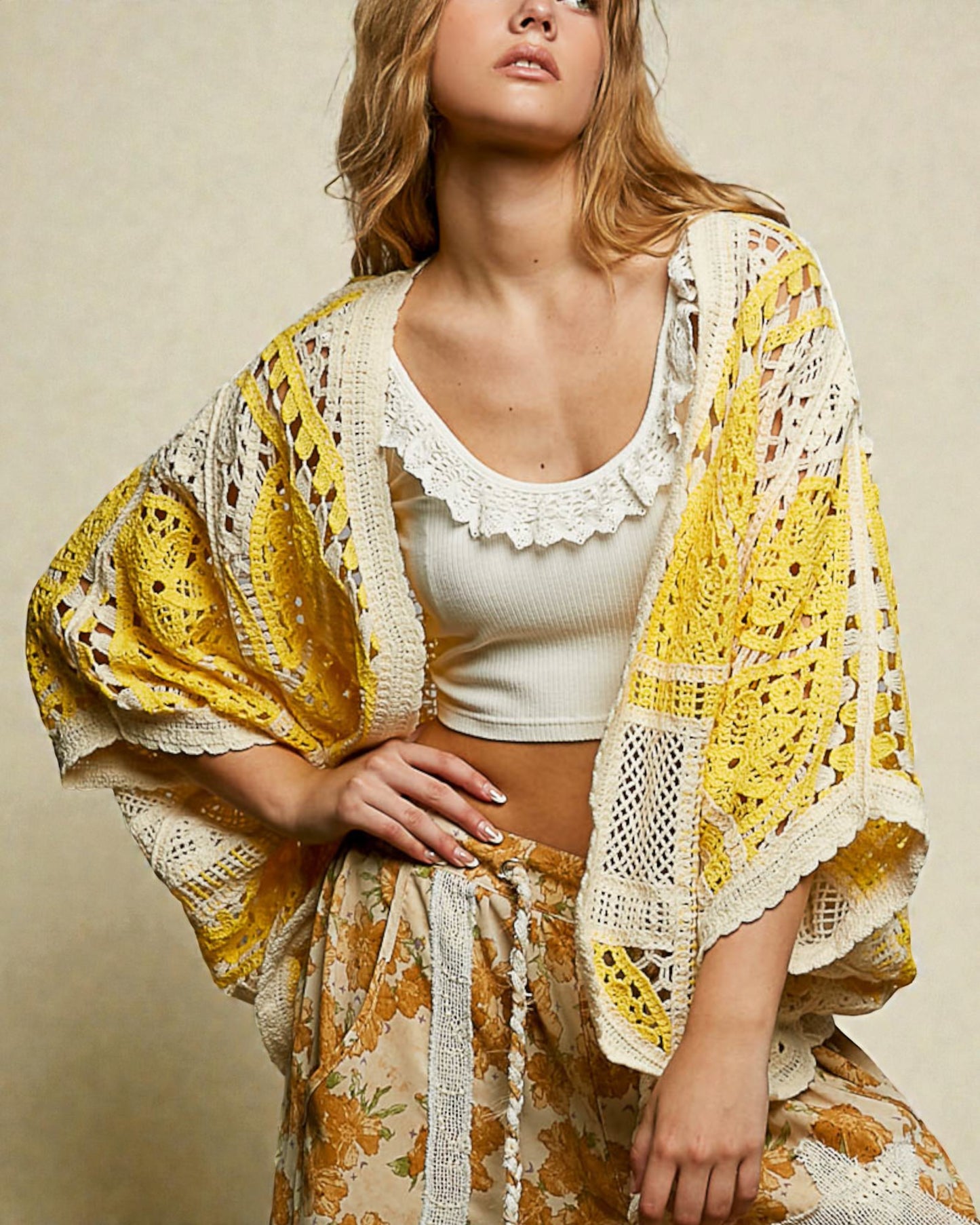 Woman wearing a yellow and white crochet cover-up over a white top against a beige background
